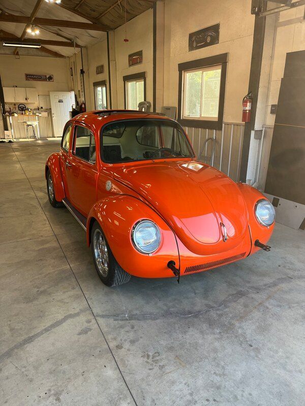 An orange volkswagen beetle is parked in a garage.