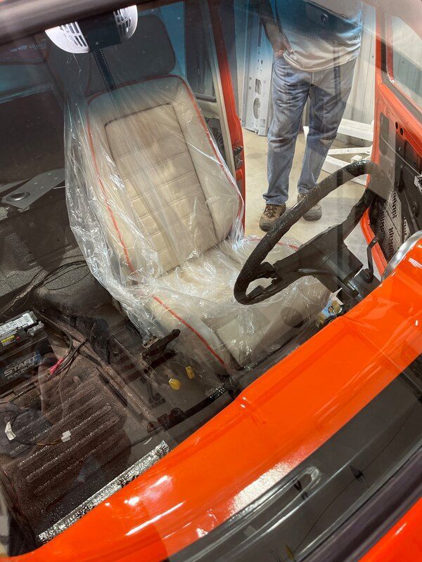 A man is standing next to an orange car with a white seat and steering wheel