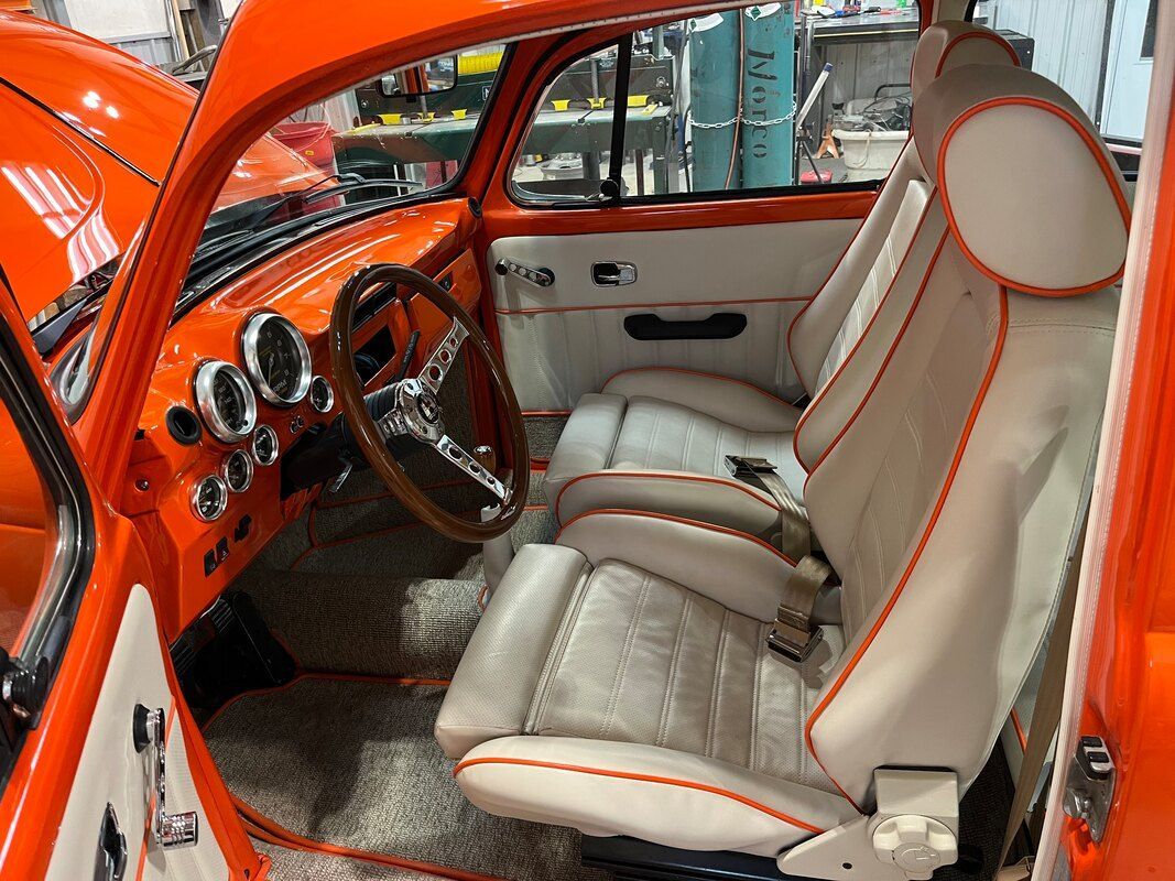 The interior of an orange car with white seats and a wooden steering wheel.