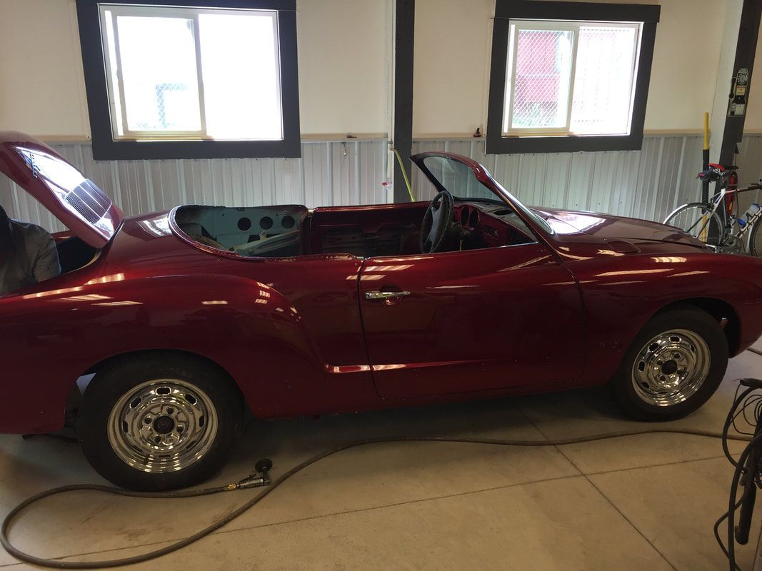 A red convertible car is parked in a garage with the hood up.