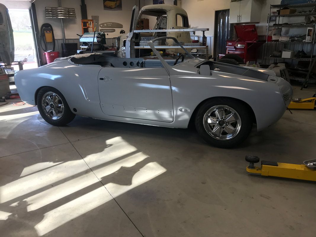A white car is parked in a garage next to a yellow jack.