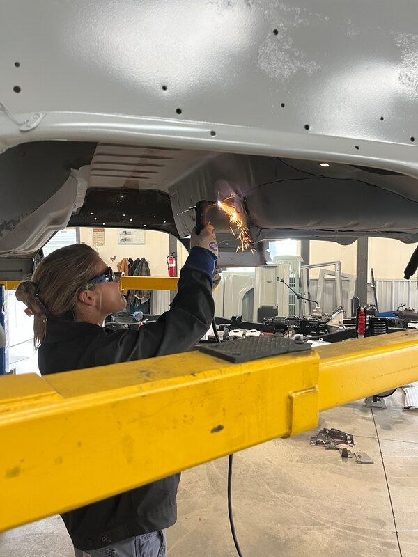 A woman is welding under the hood of a car