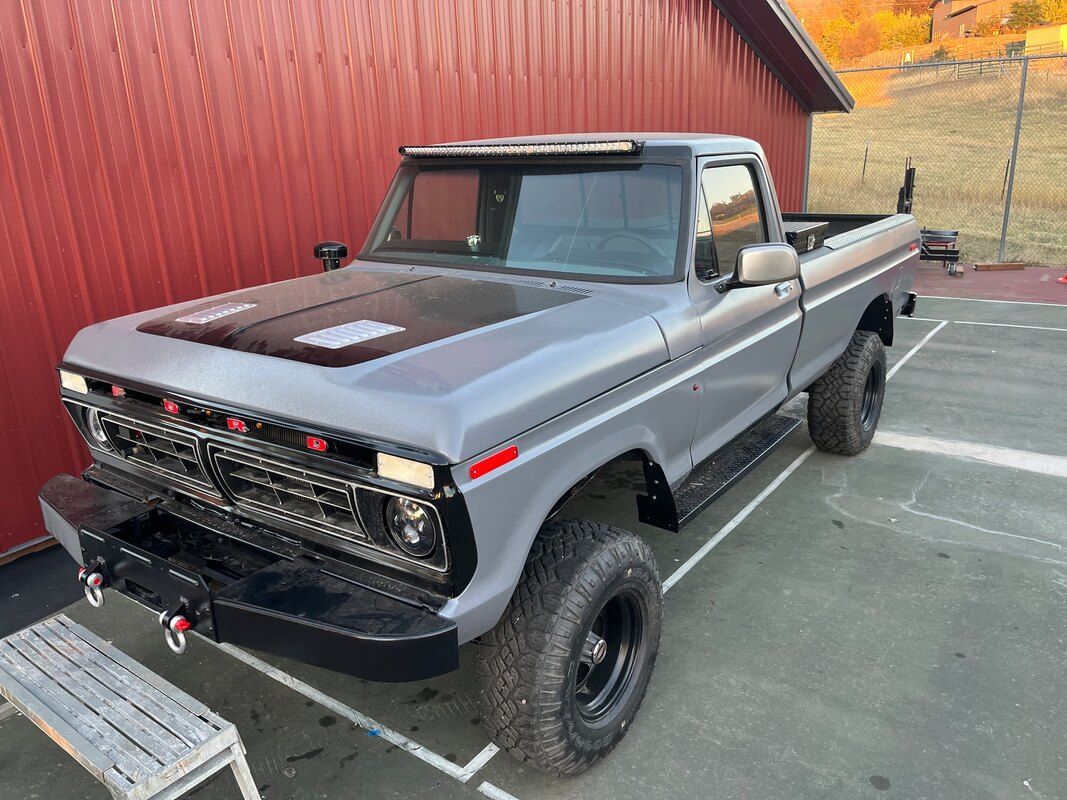 A gray truck is parked in front of a red barn.