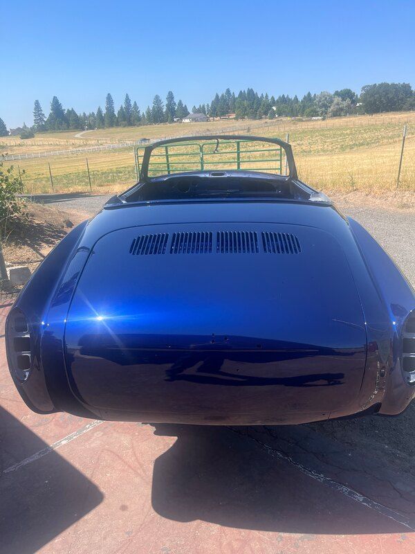 A blue car is parked in a driveway with a field in the background