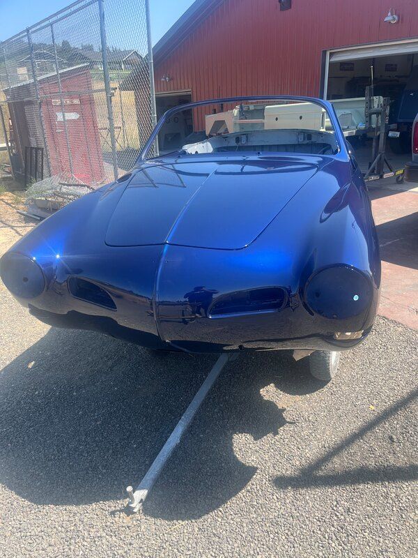 A blue car is parked in front of a red barn.