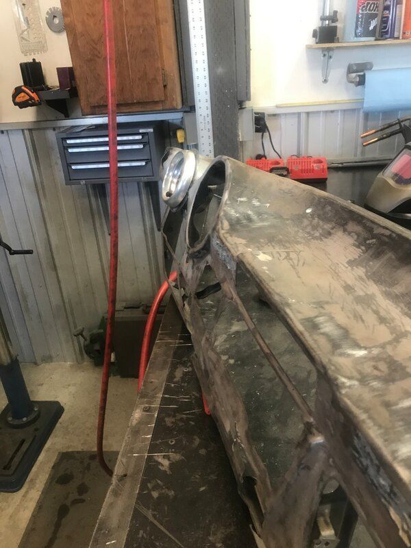 A car is being worked on in a garage with a red hose attached to it.