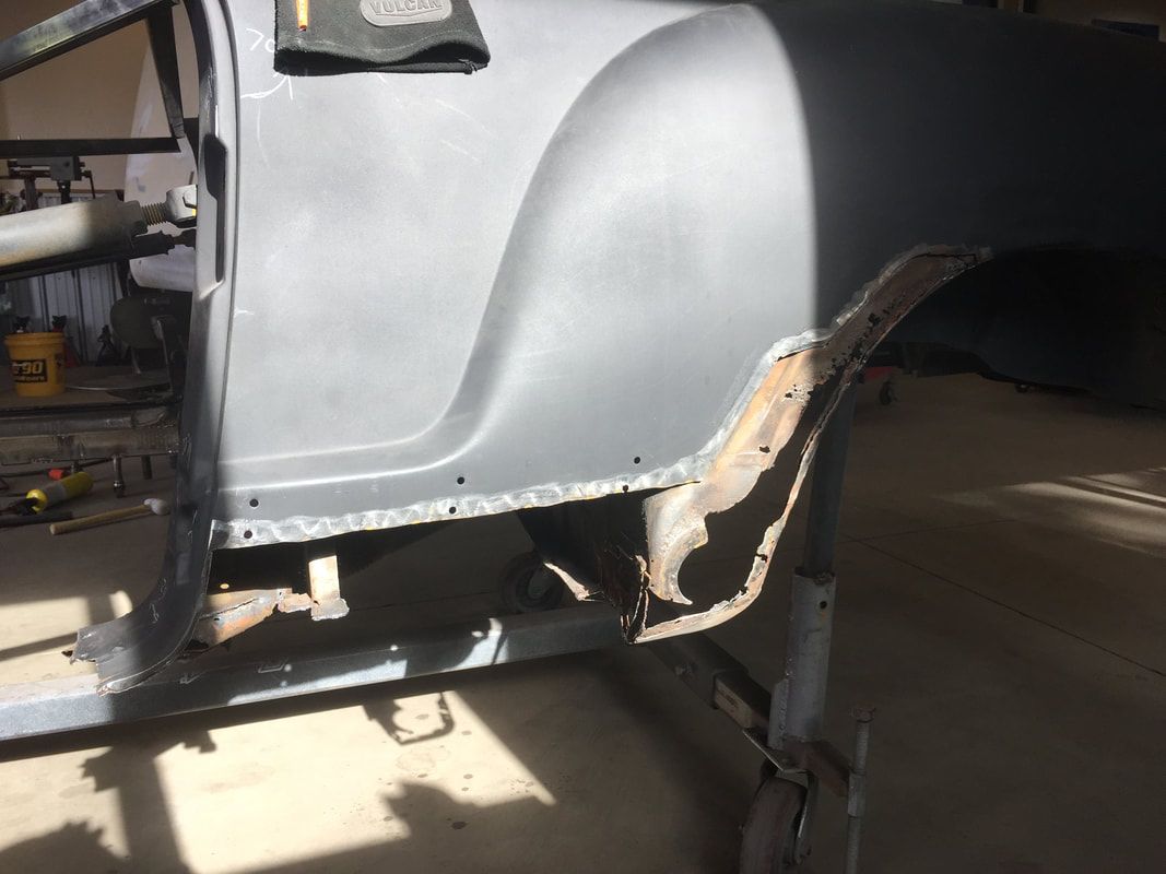 A gray car is sitting in a garage with a yellow bucket in the background.