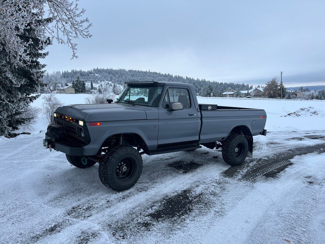 A gray truck is parked in the snow on a dirt road.