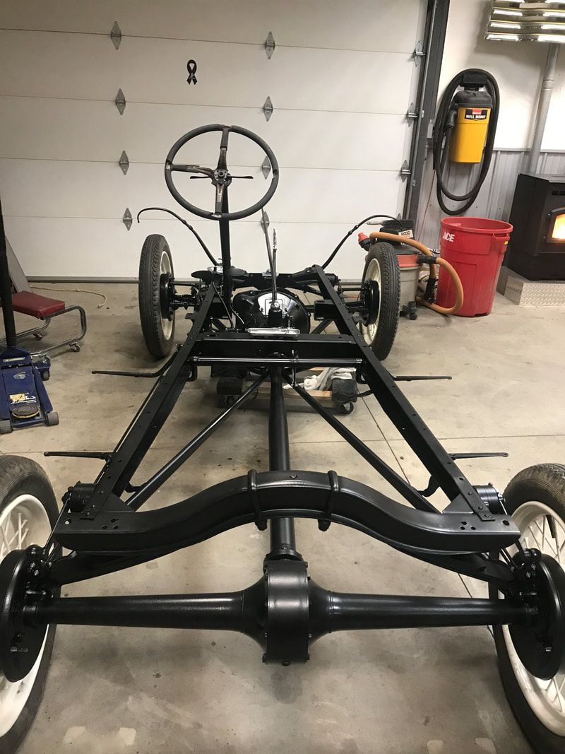 A car frame with a steering wheel is sitting in a garage.