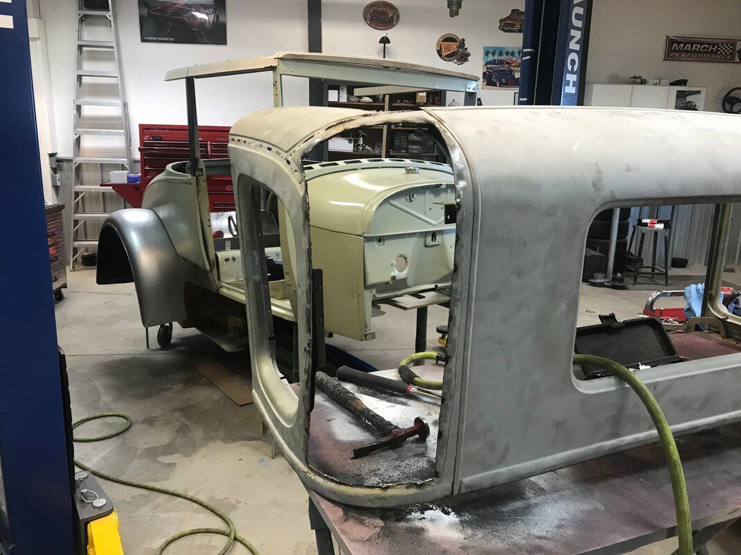 A car is being restored in a garage and is sitting on a table.