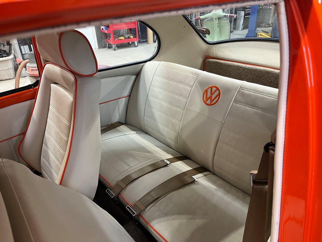 The interior of an orange vw beetle with white seats and a volkswagen logo on the back seat.