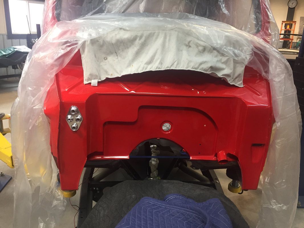 A red car is wrapped in plastic and is being worked on