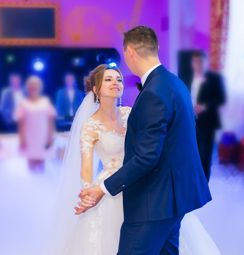 Bride and groom dancing at a colorful wedding reception, holding hands and smiling at each other