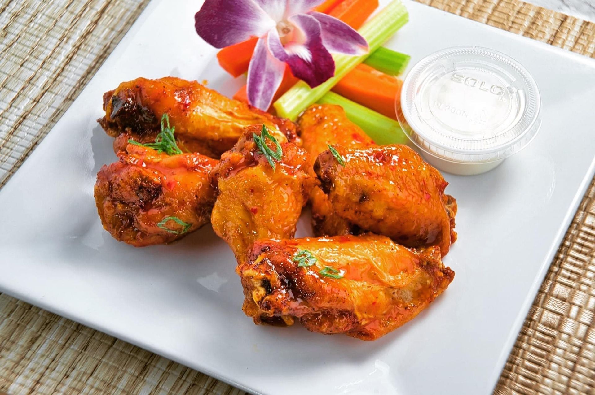 Buffalo wings on a white plate, served with carrots, celery, and ranch dressing, garnished with a flower.