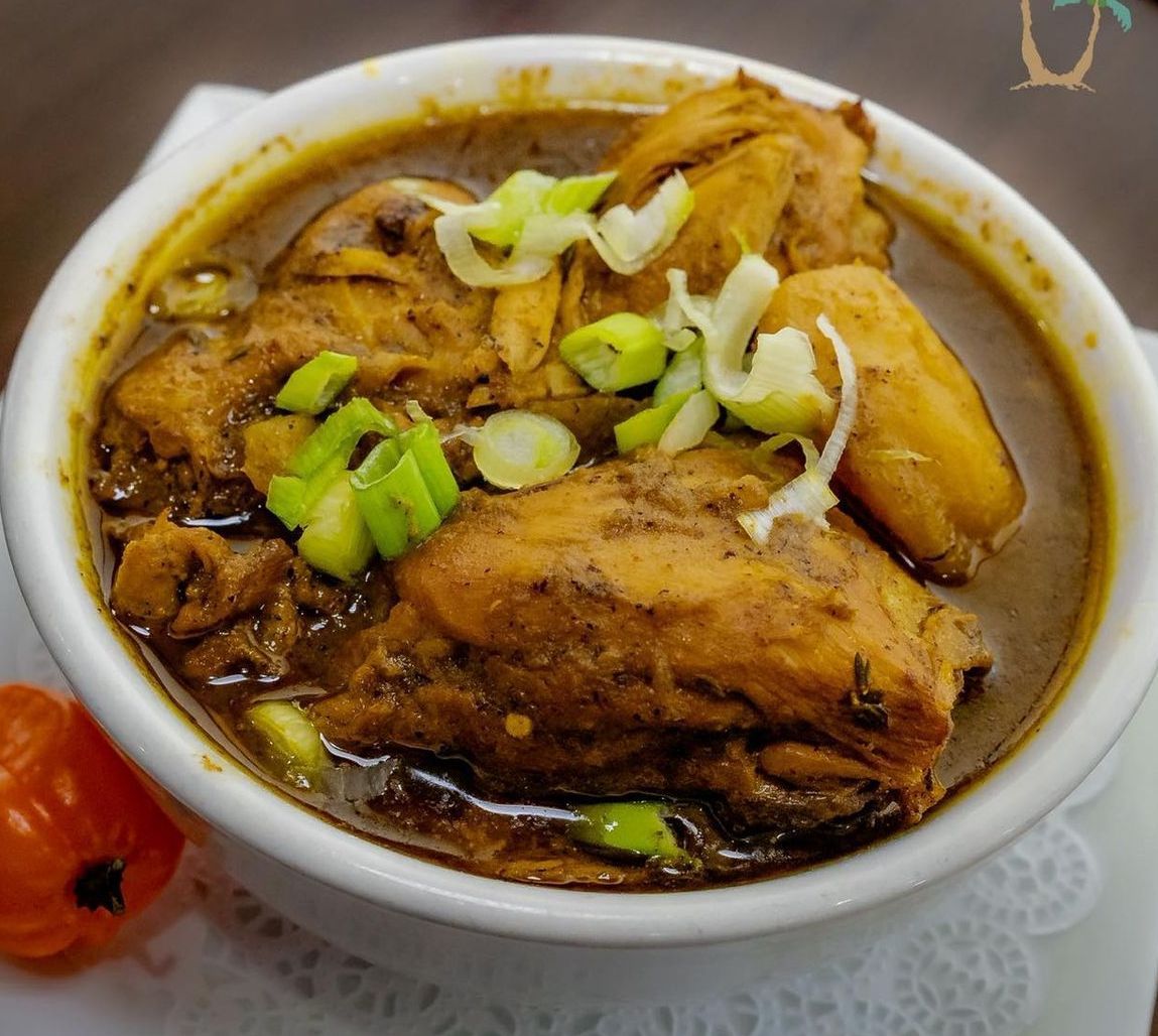 Bowl of Jamaican Brown Stew Chicken, garnished with scallions, and a red pepper on the side.