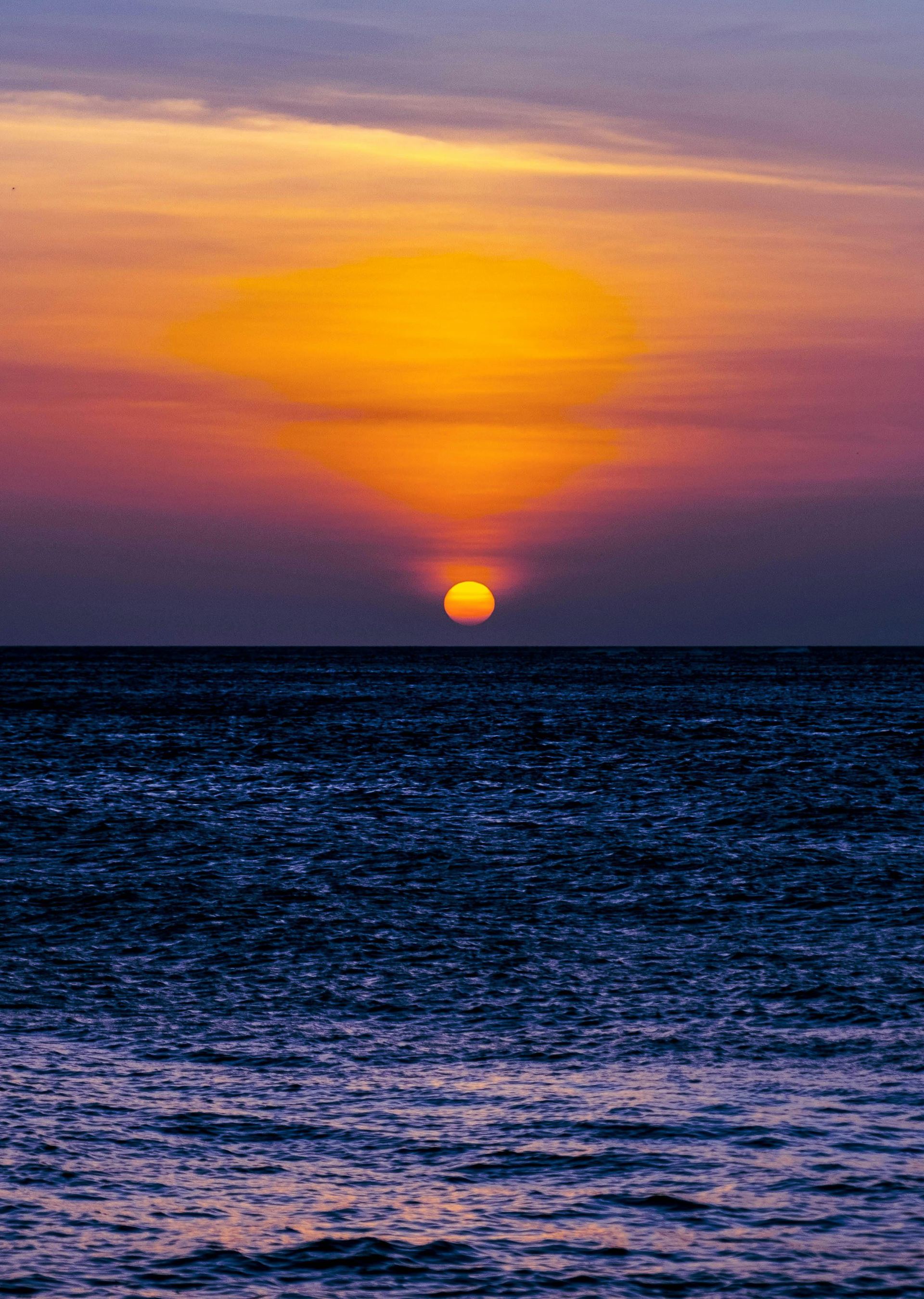 Ocean at sunset with a bright orange sun, reflecting on the water. Purple and yellow sky.