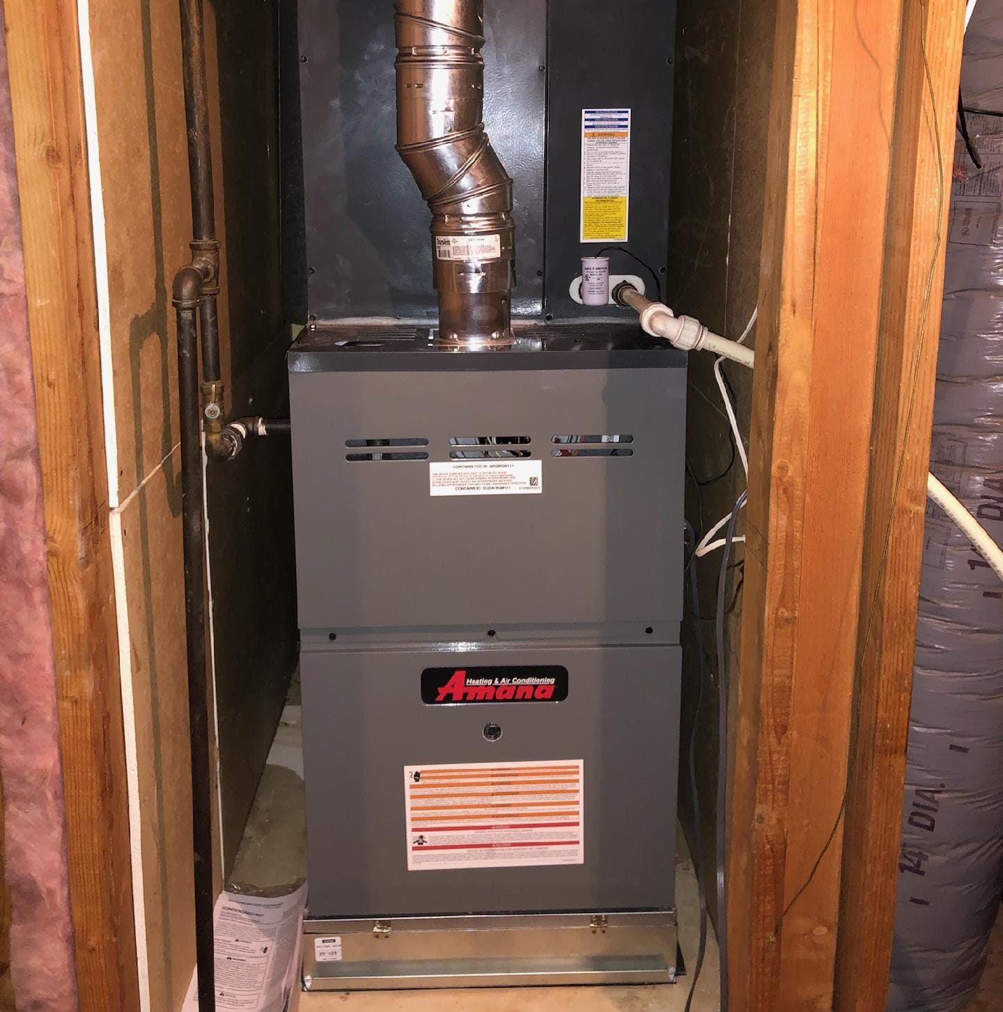 Furnace in a wooden enclosure with a vent pipe, gas line, and electrical components visible.