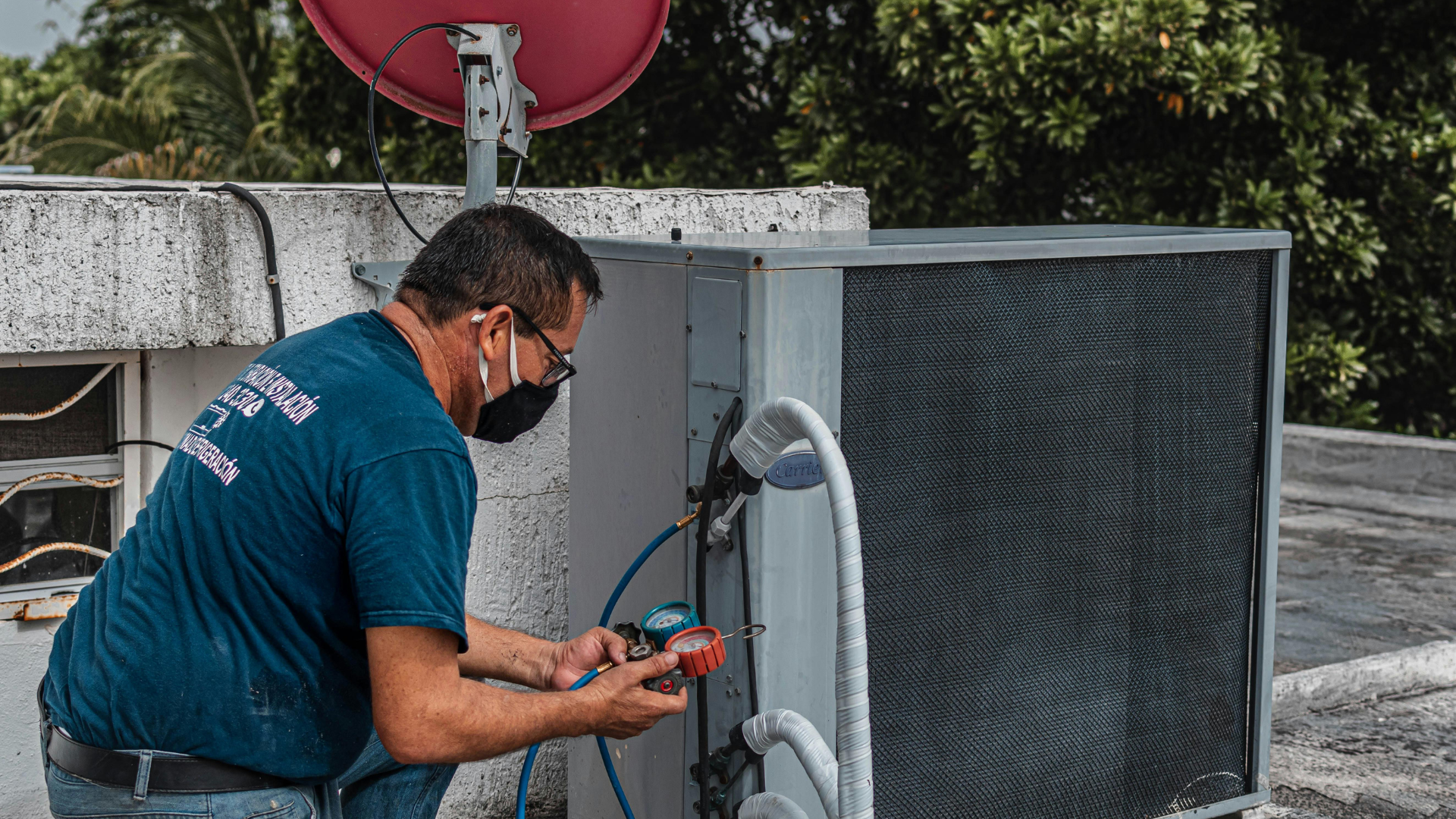HVAC technician in a mask works on an air conditioning unit on a rooftop.