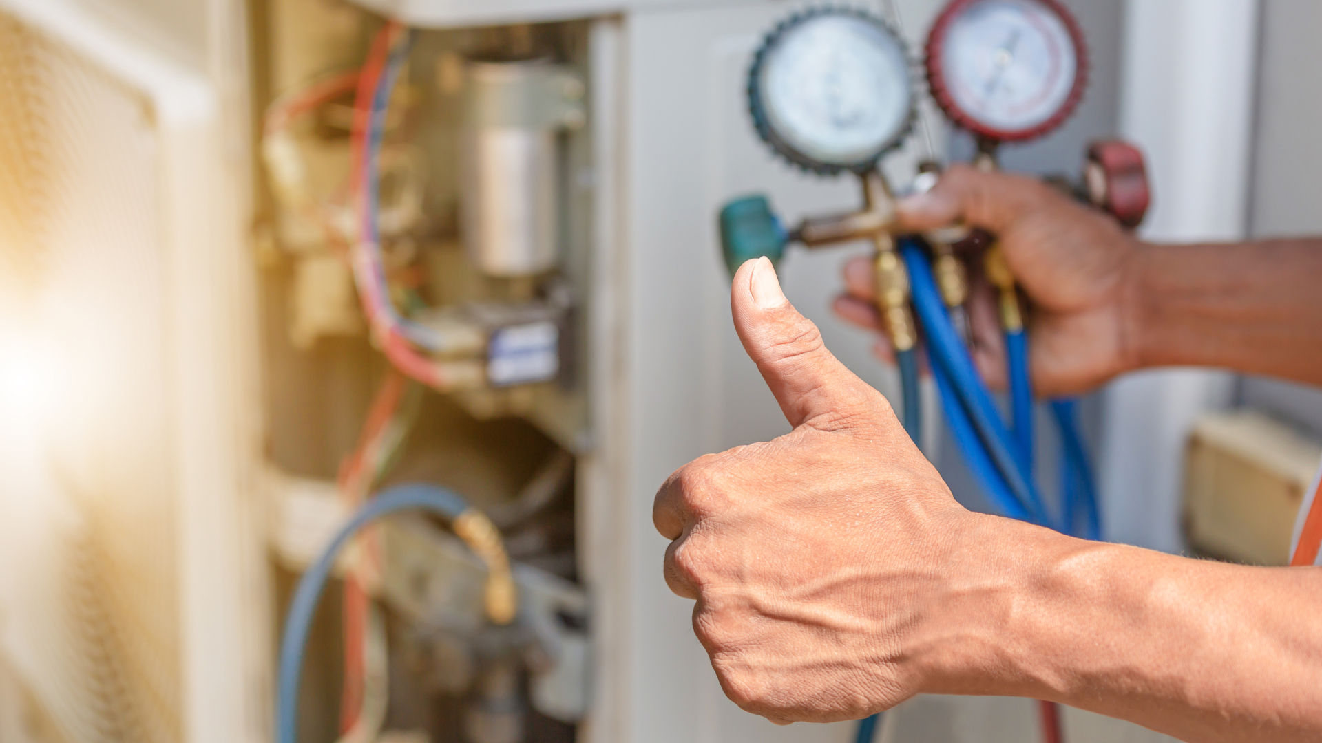 HVAC technician with thumbs up, checking gauges on an air conditioning unit.
