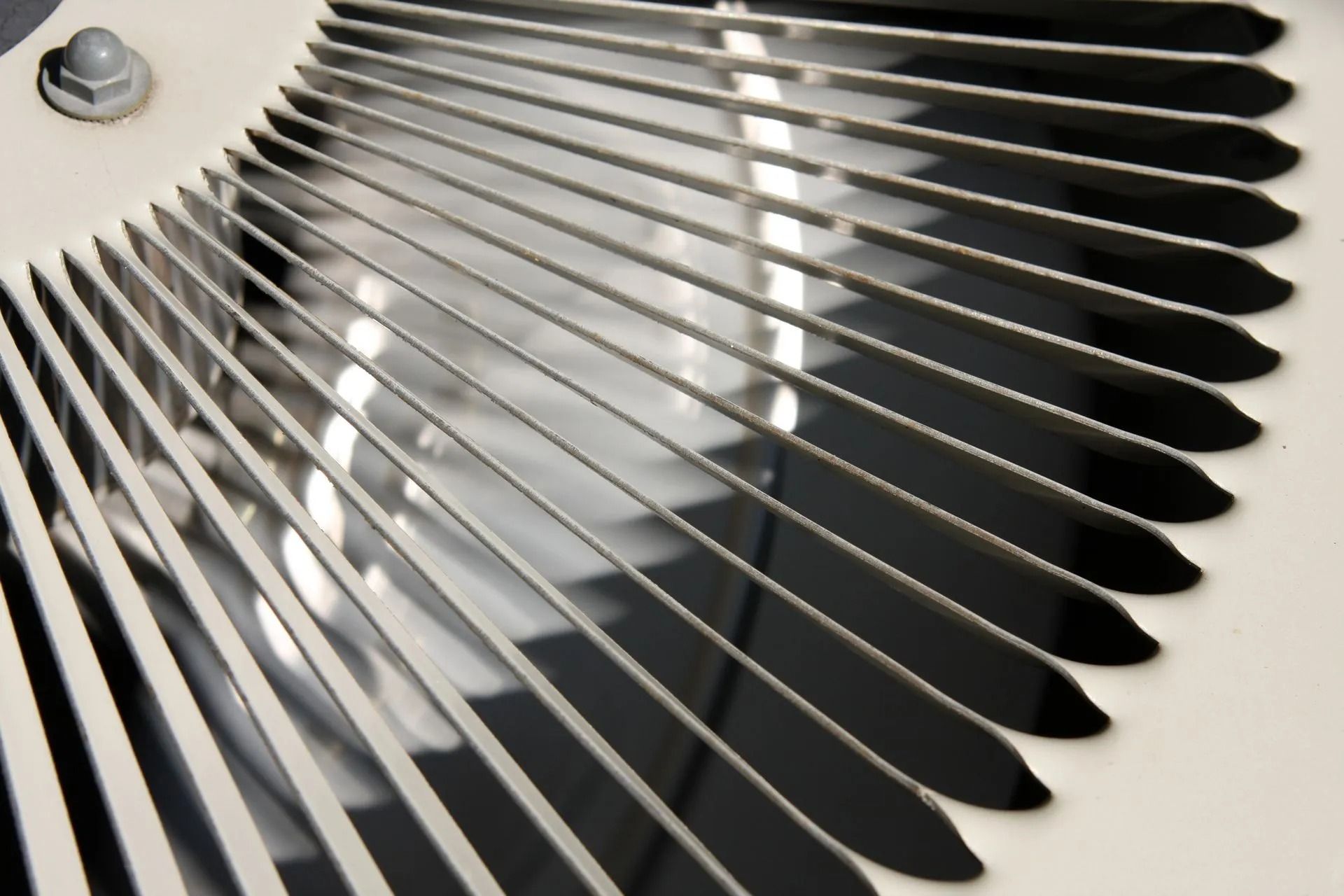 Close-up of a circular air conditioner fan with silver blades and a light gray background.
