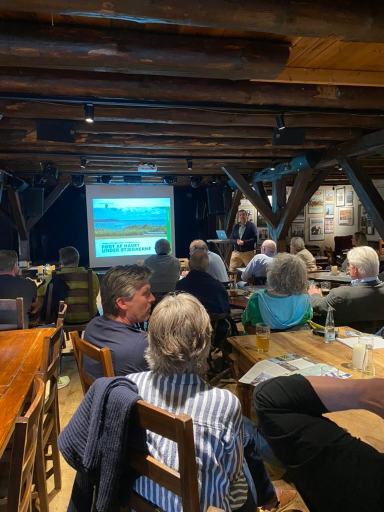 En gruppe mennesker sidder ved borde på en restaurant og ser en præsentation.