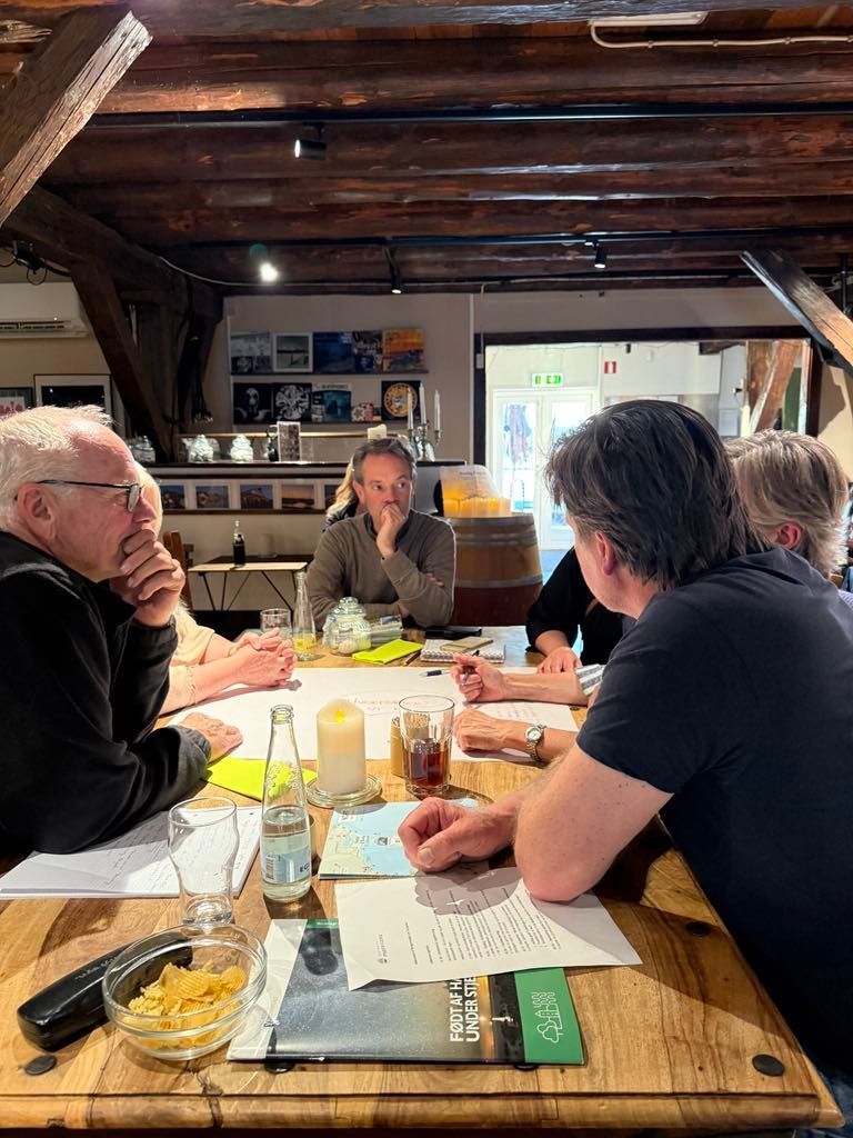 En gruppe mennesker sidder omkring et træbord i et rum.