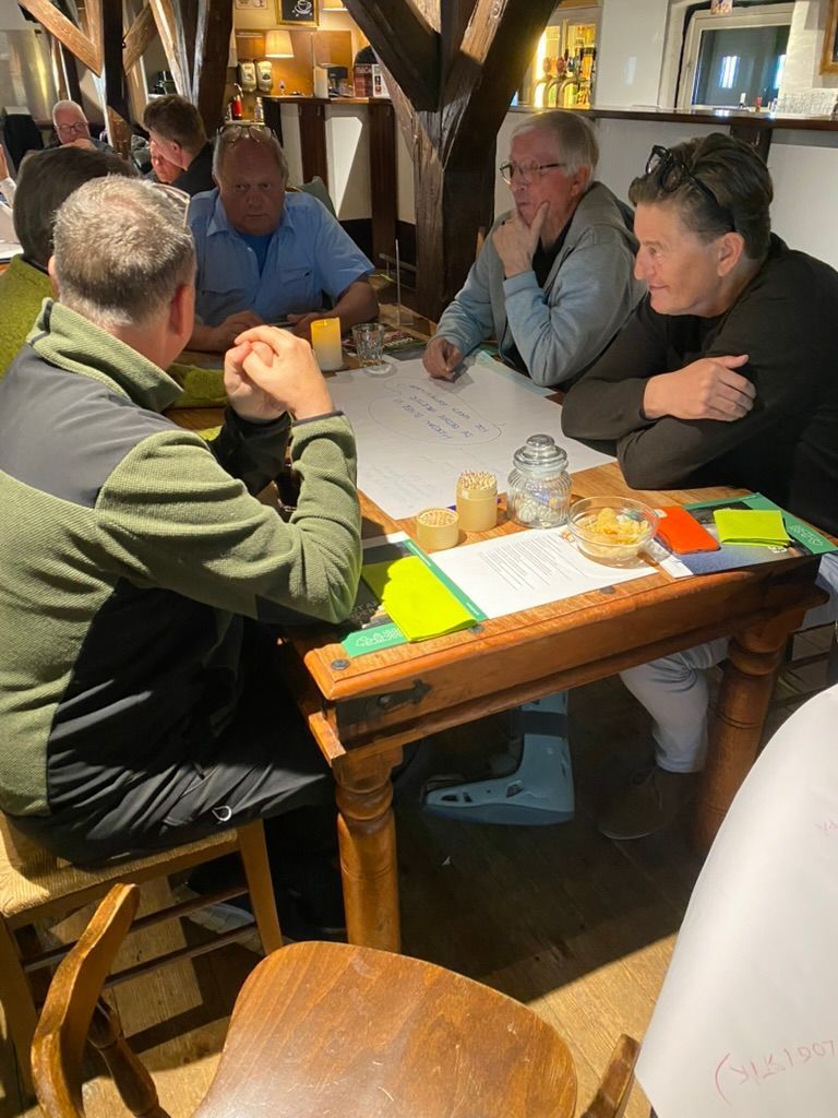 En gruppe mennesker sidder omkring et bord med sedler på.