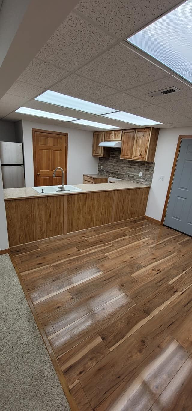 A living room with hardwood floors and a kitchen in the background.