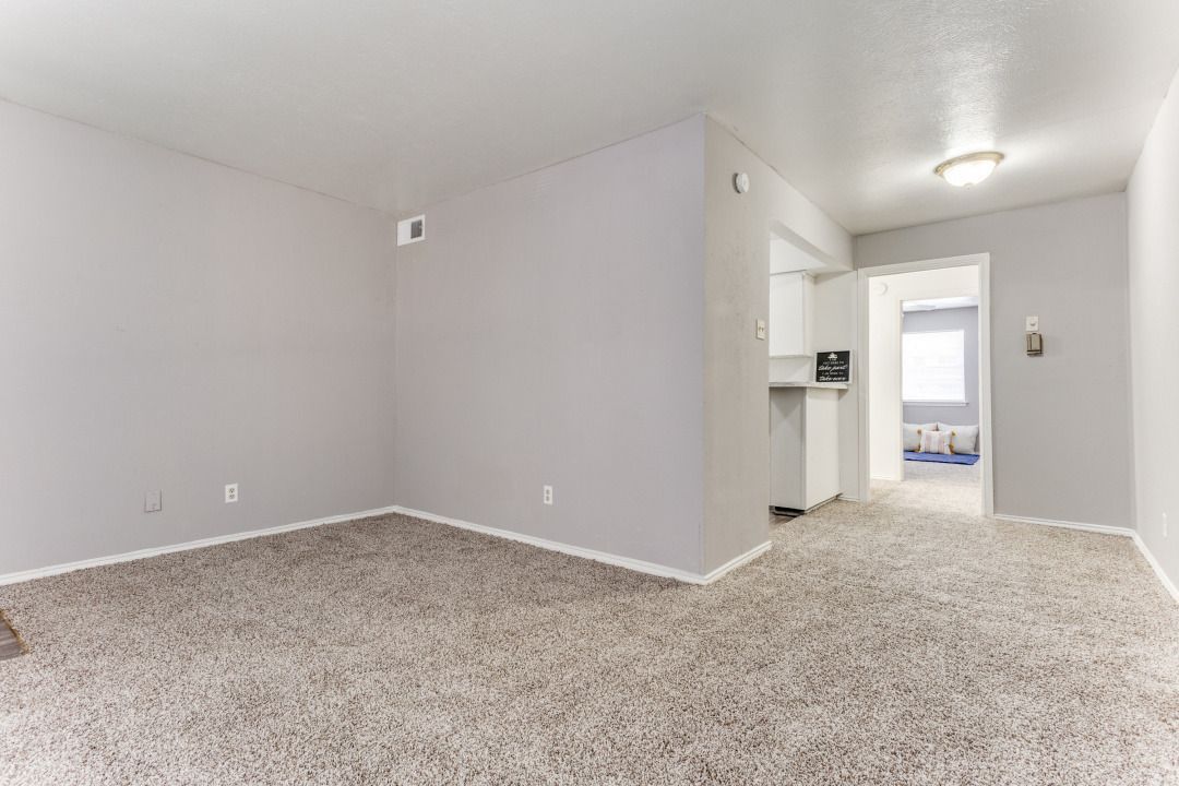 An empty living room with a carpeted floor and white walls.