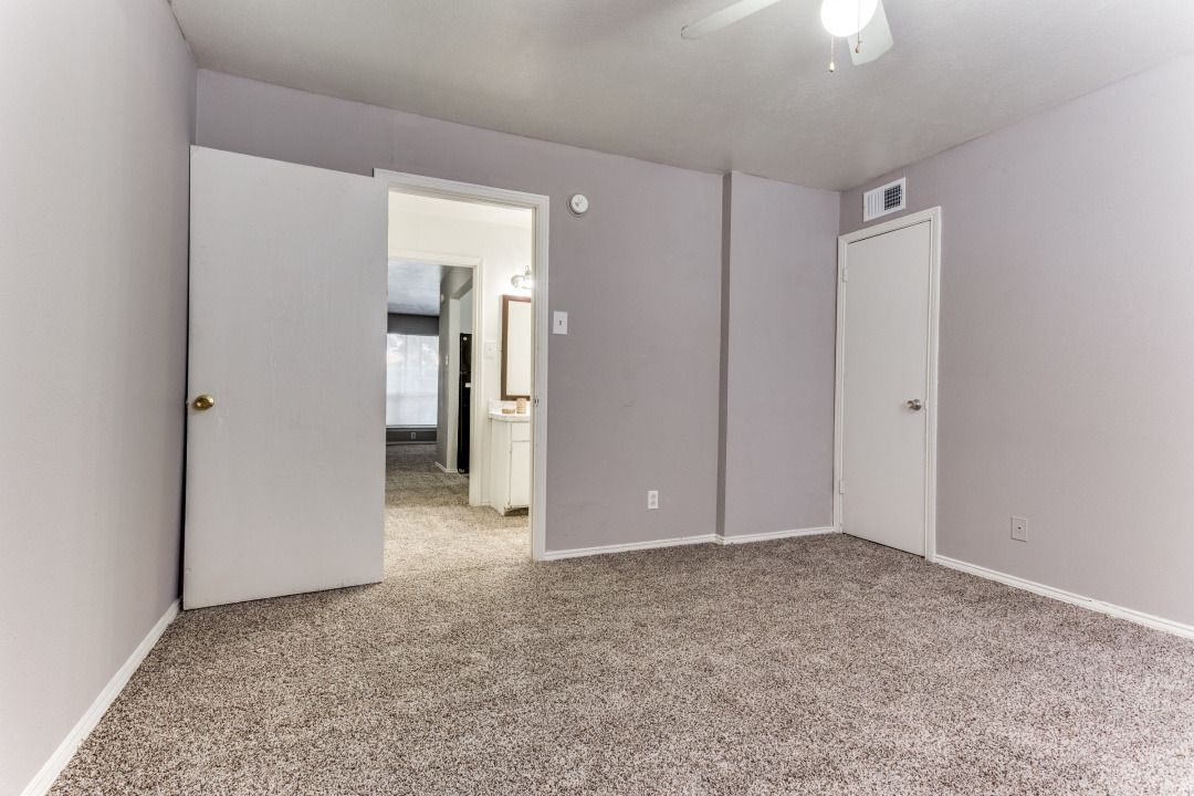 An empty bedroom with a carpeted floor and a ceiling fan.