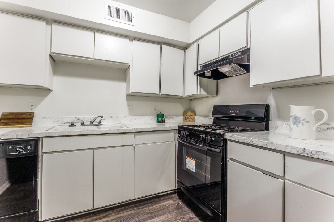 A kitchen with white cabinets , a stove , a dishwasher , and a sink.