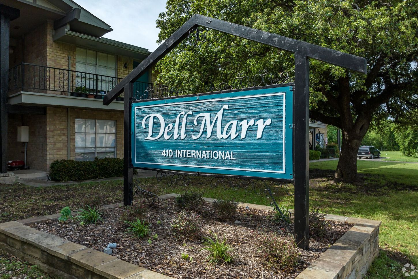 A sign for del marr apartments is sitting in front of a brick building.