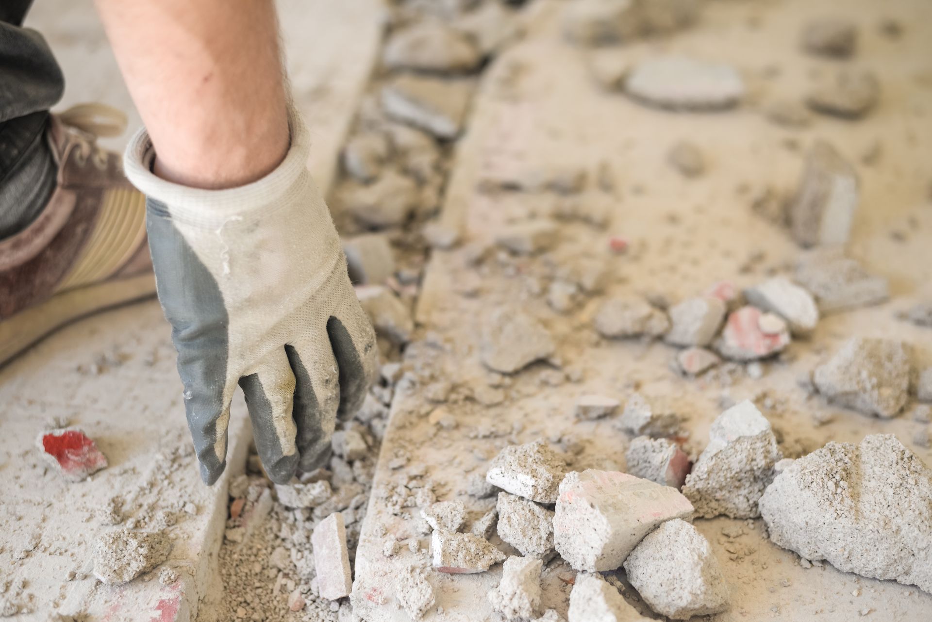 A person wearing a work glove cleans debris from a construction site.