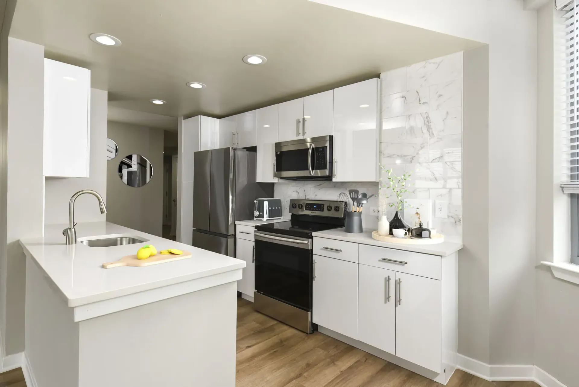 Modern white kitchen with stainless steel appliances, an island sink, and marble backsplash.