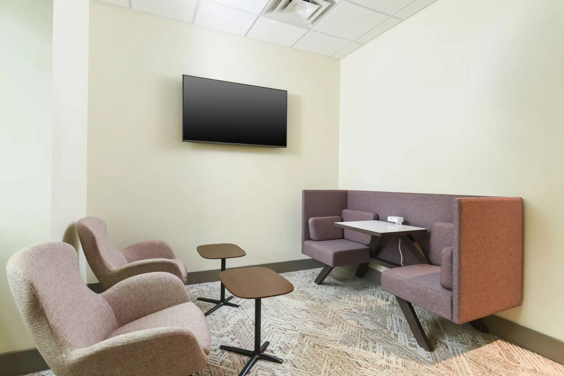 Common lounge area with wall-mounted TV, purple seating, and small tables.