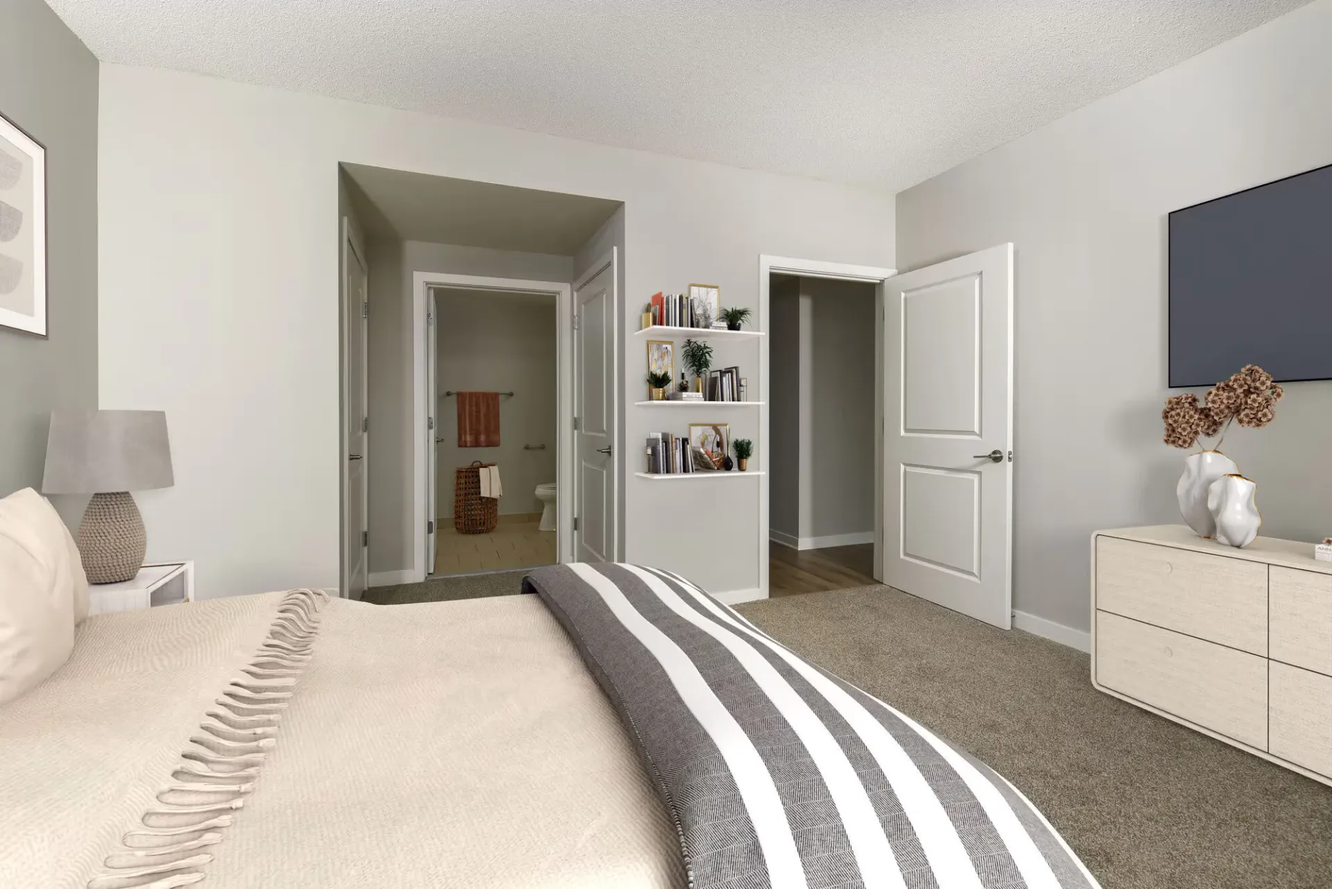 Furnished apartment bedroom with bed, dresser, wall-mounted TV, and an open doorway to the bathroom.