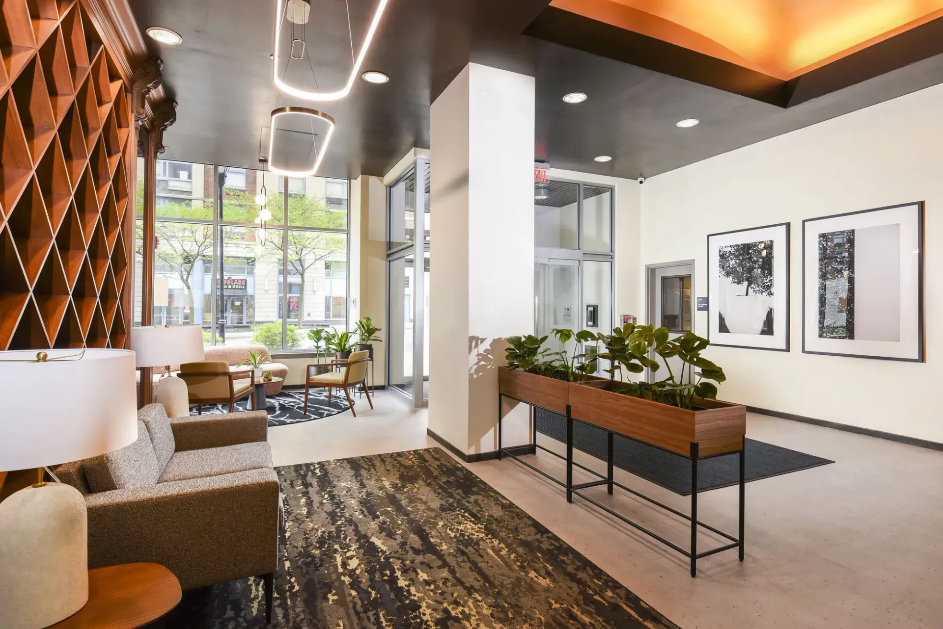 Modern apartment lobby with lounge seating, plants, and large street-facing windows.