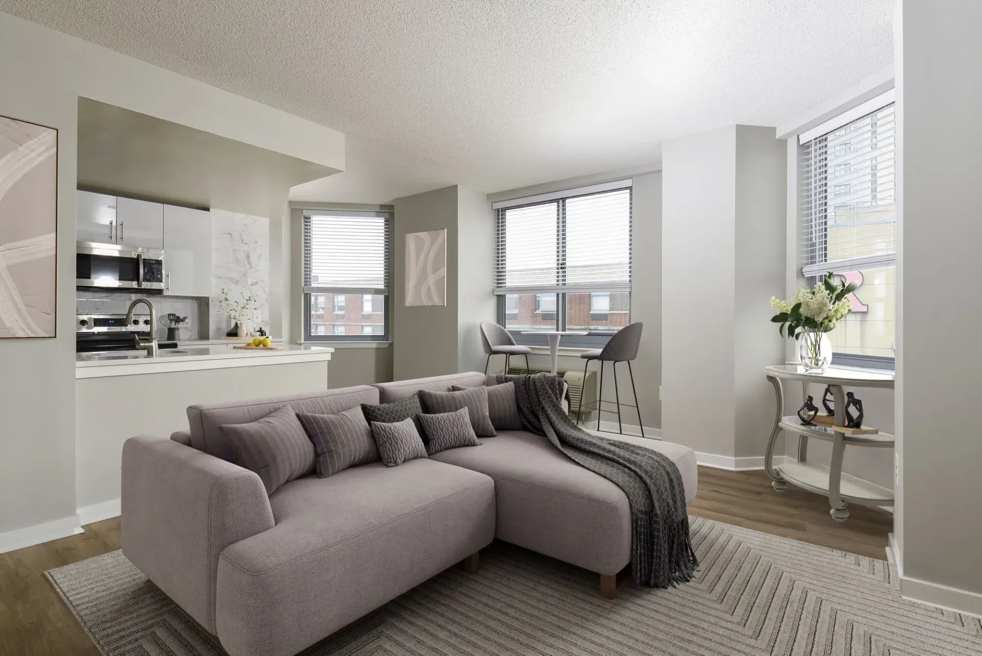 Open-concept living room with a gray sectional sofa, modern kitchen, and large windows.