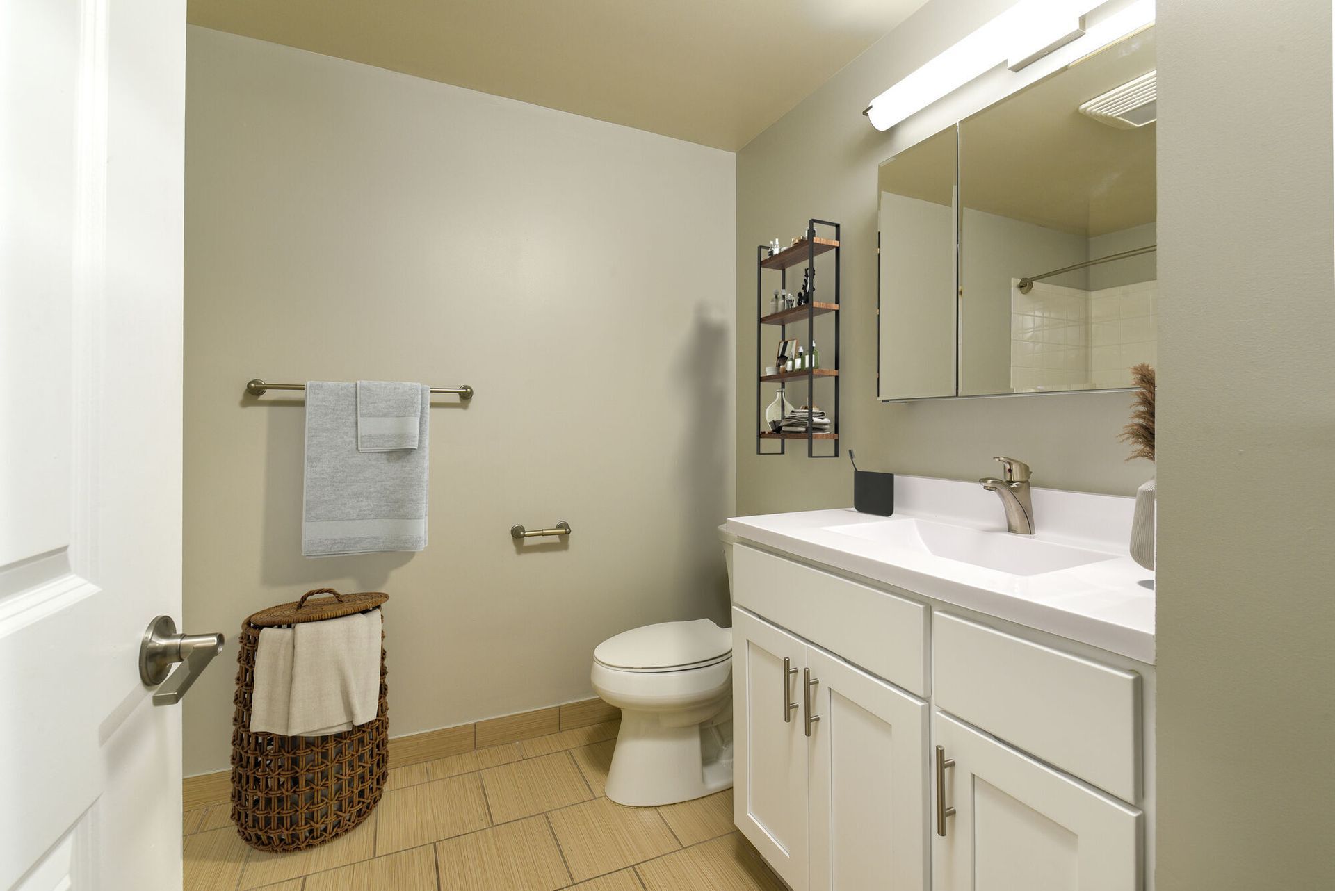 Bathroom in an apartment with a white vanity, mirror, toilet, towel rack, and shelving.