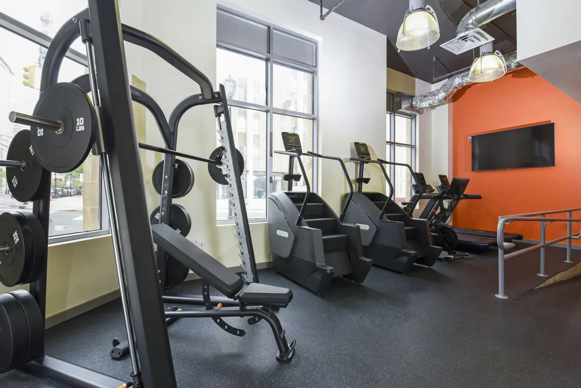 Fitness center with cardio machines and free weights near large windows.