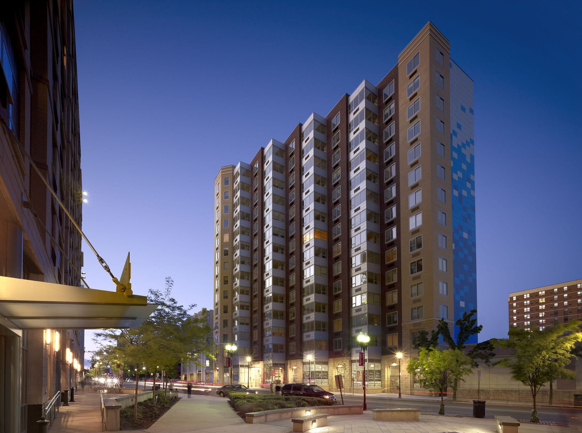 Exterior view of a modern apartment building at dusk with streetlights and trees.