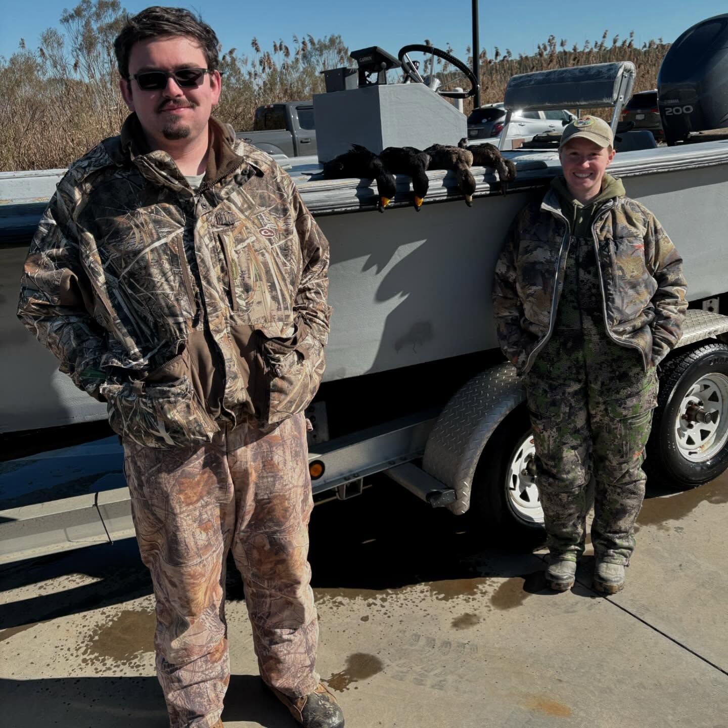 Two men in camo standing next to a boat