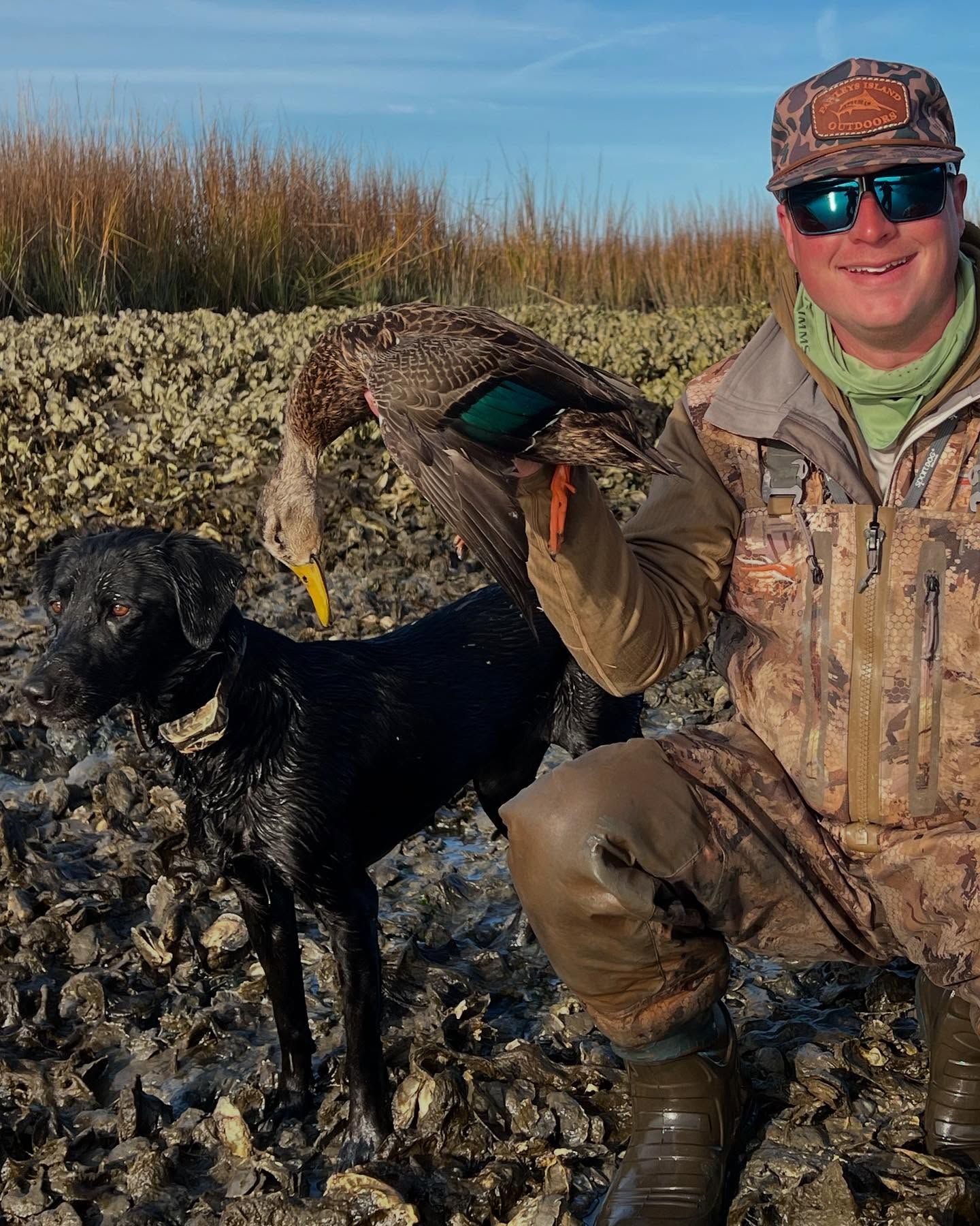 A man holding a duck next to a black dog