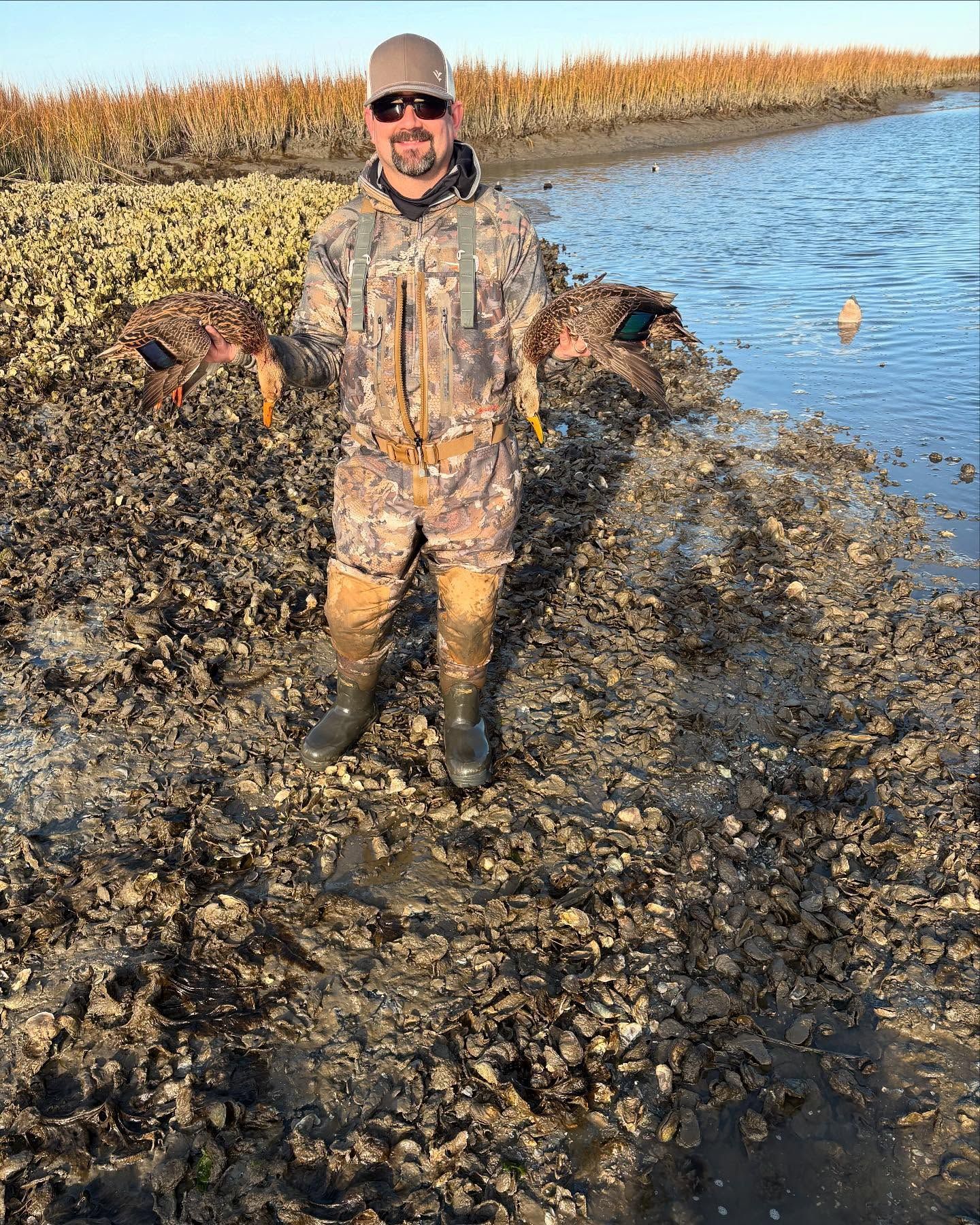 A man is standing in the mud holding a duck.