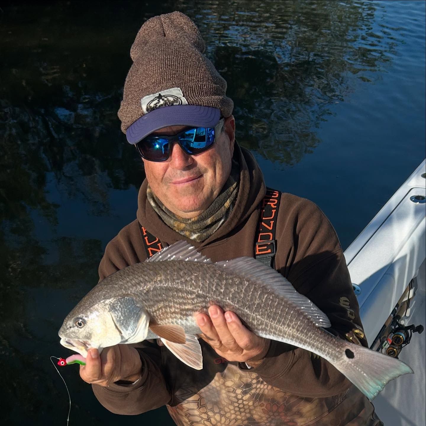 A man wearing a hat and sunglasses is holding a fish