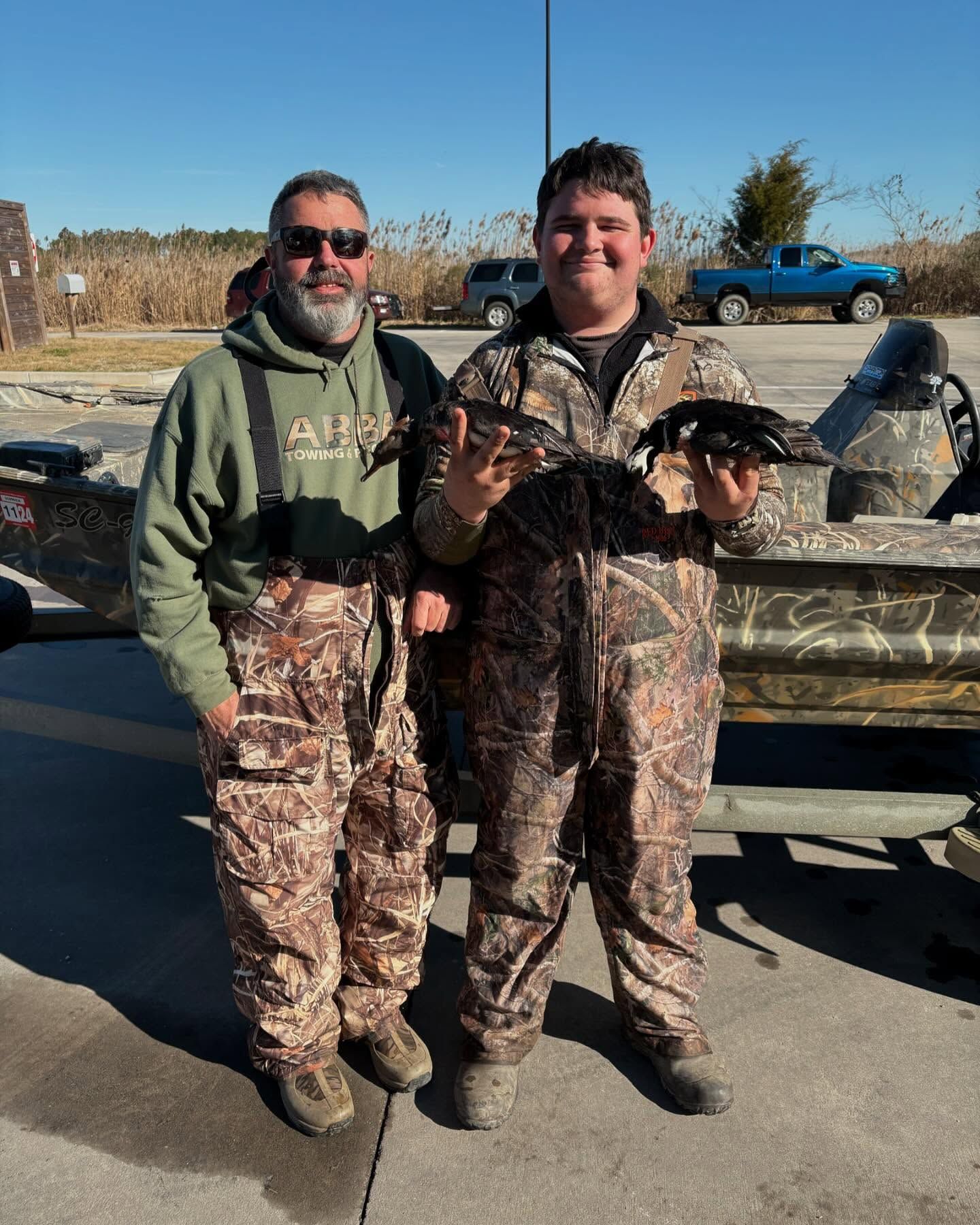 Two men in camouflage standing next to each other holding fish