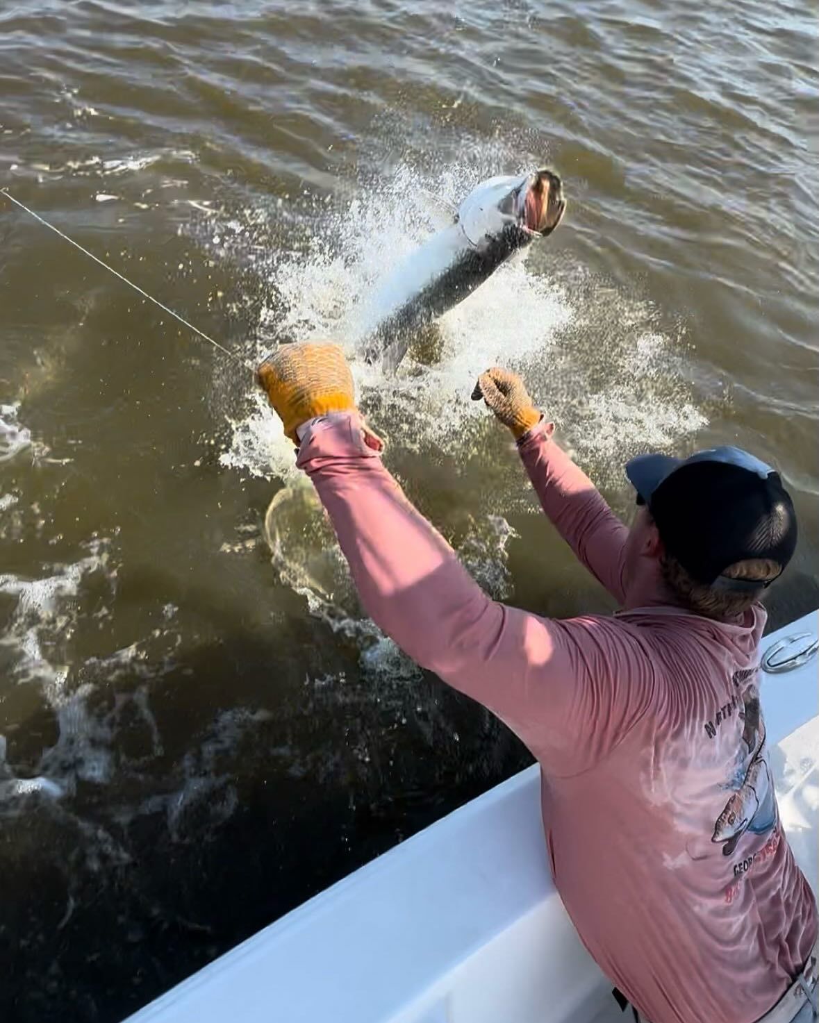 A man in a pink shirt is fishing in the water