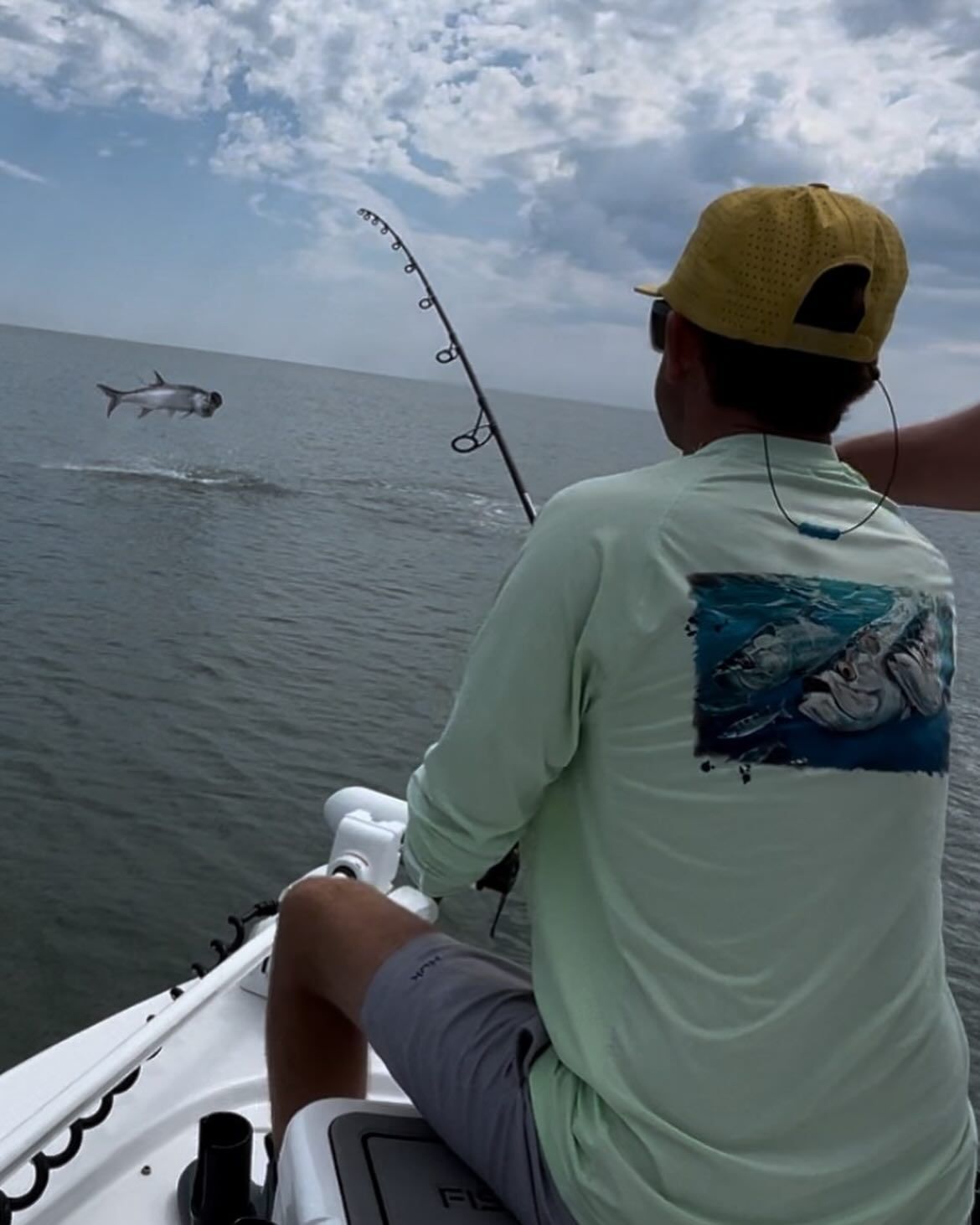 A man in a green shirt is fishing in the ocean