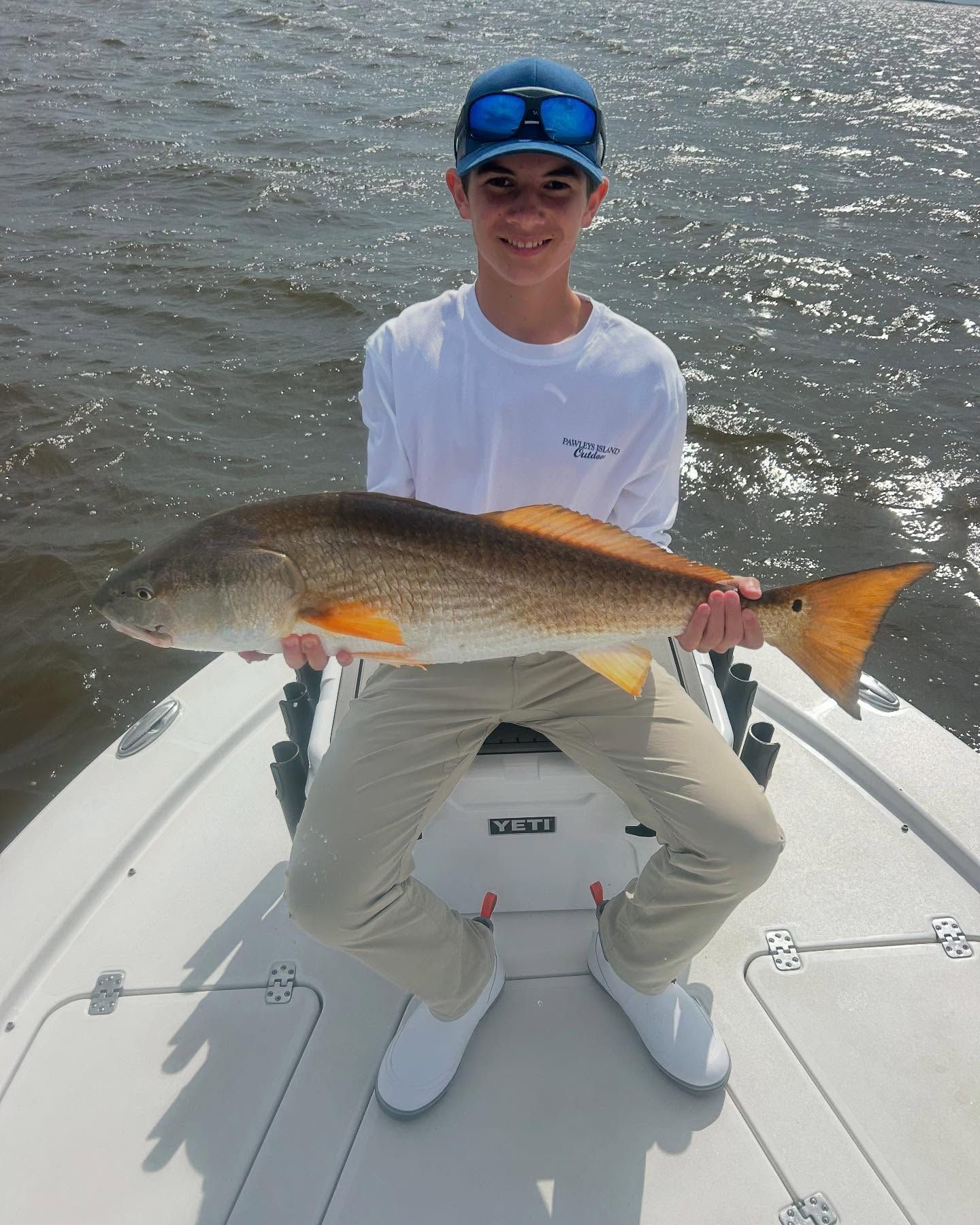 A young man is sitting on a boat holding a large fish