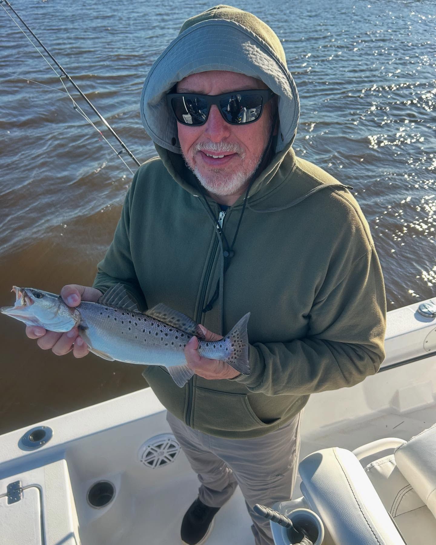 A man in a hoodie is holding a fish on a boat.